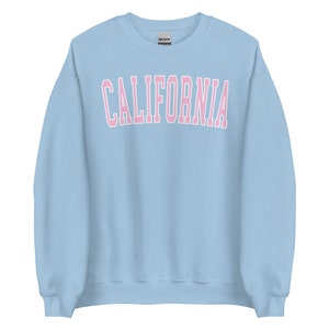 K&ouml;nnte beinhalten: Ein hellblauer Pullover mit dem Wort "CALIFORNIA" in rosa Buchstaben mit wei&szlig;em Umriss.