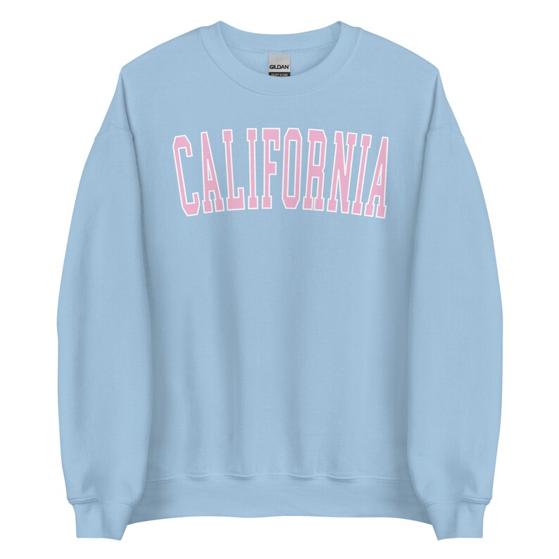 K&ouml;nnte beinhalten: Ein hellblauer Pullover mit dem Wort "CALIFORNIA" in rosa Buchstaben mit wei&szlig;em Umriss.