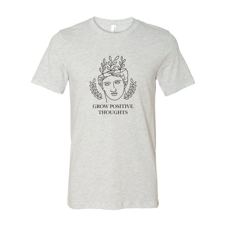 May include: A heather grey t-shirt with a black line drawing of a person with leaves growing from their head. The text "GROW POSITIVE THOUGHTS" is printed below the drawing.