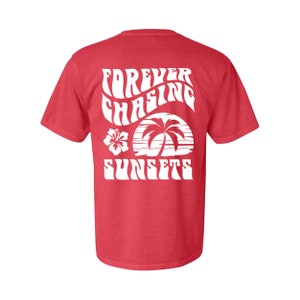 May include: Red t-shirt with a white graphic design that says "FOREVER CHASING SUNSETS" with a palm tree and hibiscus flower.
