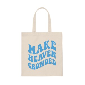 May include: A natural canvas tote bag with blue text that reads "MAKE HEAVEN CROWDED".