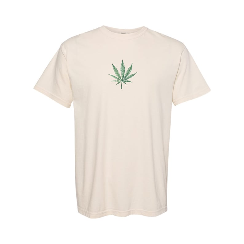 以下が含まれることがあります： 緑色のマリファナの葉のグラフィックが描かれたクリーム色のTシャツ