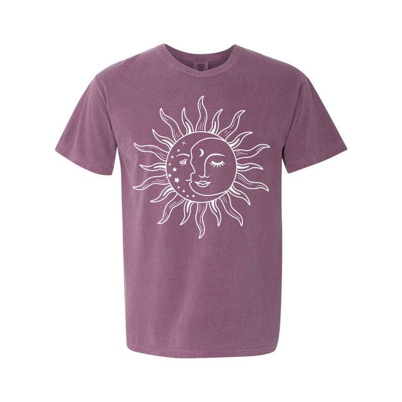 K&ouml;nnte beinhalten: Ein kurz&auml;rmliges T-Shirt in Lila mit einem wei&szlig;en Sonnen- und Mondmotiv. Die Sonne hat ein Gesicht und der Mond hat eine sichelf&ouml;rmige Form mit Sternen.