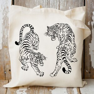 May include: A white tote bag with a black and white illustration of two tigers facing each other. The tigers are drawn in a stylized, almost Japanese-inspired style.