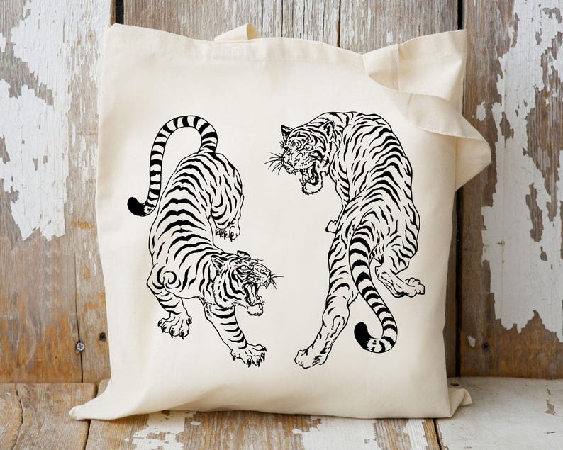 May include: A white tote bag with a black and white illustration of two tigers facing each other. The tigers are drawn in a stylized, almost Japanese-inspired style.