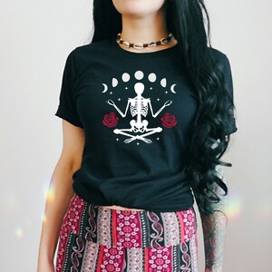 May include: Black t-shirt with a white skeleton meditating with red roses and a crescent moon design. The text "Shroom Queens" is printed on the shirt.
