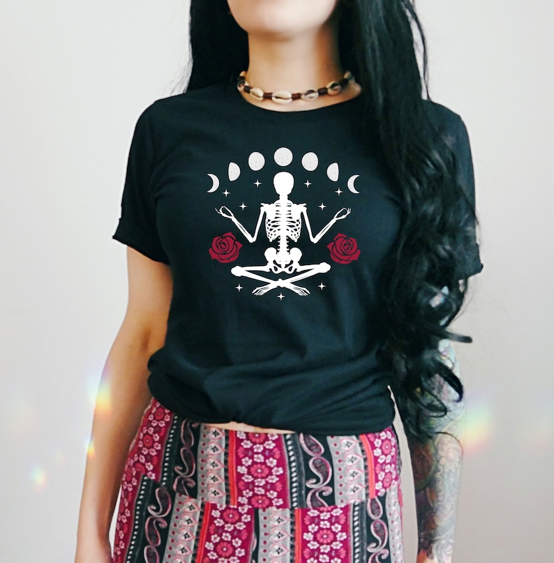 May include: Black t-shirt with a white skeleton meditating with red roses and a crescent moon design. The text "Shroom Queens" is printed on the shirt.