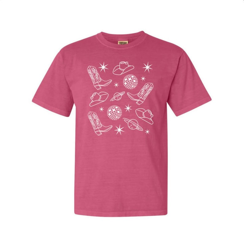 Puede incluir: Una camiseta rosa con un dise&ntilde;o blanco de botas de vaquero, sombreros, bolas de discoteca y estrellas.