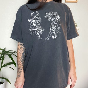 May include: A charcoal gray oversized t-shirt with a white graphic print of two tigers facing each other. The text "Pepper" is printed on the bottom of the shirt.