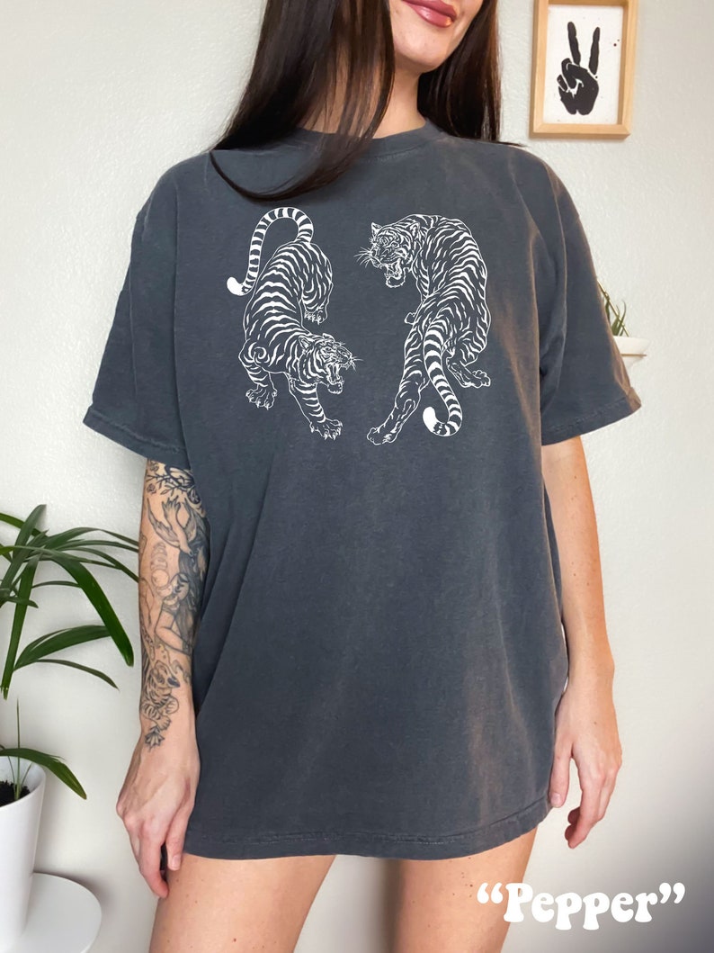 May include: A charcoal gray oversized t-shirt with a white graphic print of two tigers facing each other. The text "Pepper" is printed on the bottom of the shirt.
