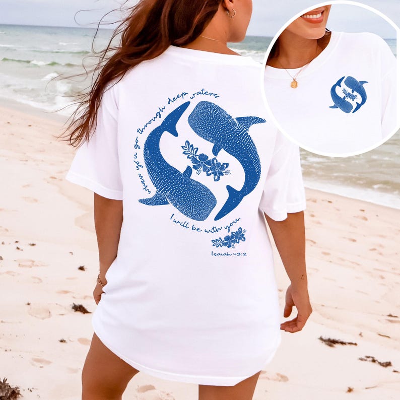 K&ouml;nnte beinhalten: Ein wei&szlig;es T-Shirt mit einer blauen Grafik von zwei Walhaien und Hibiskusbl&uuml;ten auf der R&uuml;ckseite, inklusive des Textes "when you go through deep waters I will be with you. Isaiah 43:2". Die Vorderseite zeigt eine kleine blaue Walhai-Grafik.