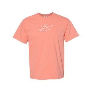 May include: A coral pink short-sleeved t-shirt with a white wave graphic on the front.