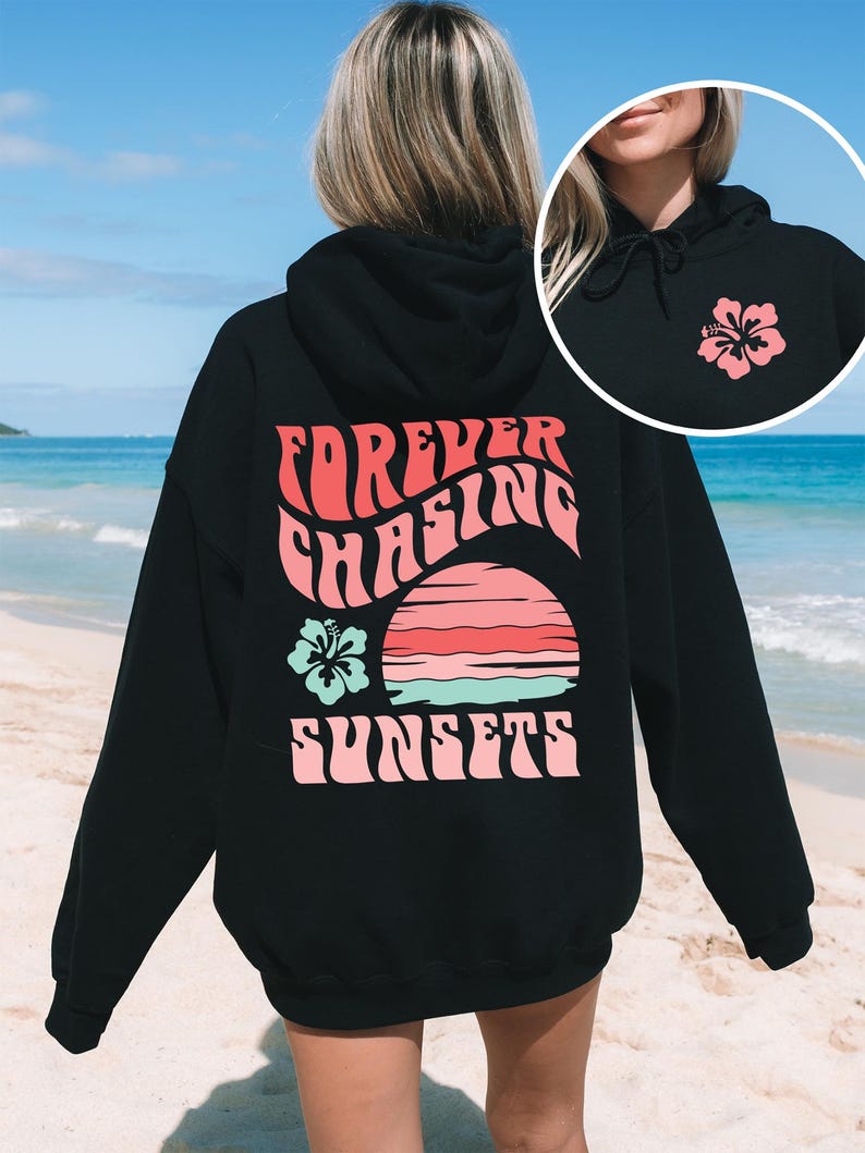 Pode incluir: Um moletom preto com capuz apresentando um gr&aacute;fico nas costas com o texto "FOREVER CHASING SUNSETS" em rosa, um p&ocirc;r do sol estilizado em rosa e turquesa, e uma flor de hibisco turquesa. A parte frontal inclui uma pequena flor de hibisco rosa.