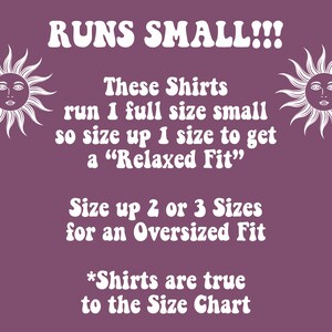 May include: A purple background with white text that reads "RUNS SMALL!!!" and instructions on sizing up for shirts. Two sun illustrations flank the text. The text advises sizing up for a relaxed or oversized fit.