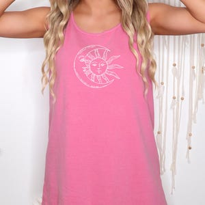 May include: A sleeveless pink tank top with a white sun and moon graphic. The sun has a face and rays, and the moon is a crescent shape. The top is made of a soft material and has a relaxed fit.