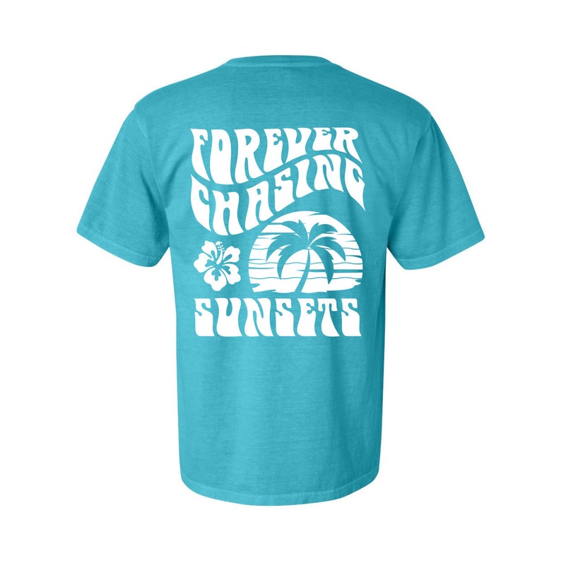 May include: A turquoise blue t-shirt with a white graphic print of a palm tree, sunset, and hibiscus flower. The text on the shirt reads "FOREVER CHASING SUNSETS".