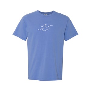 May include: A light blue t-shirt with a white wave design on the front.