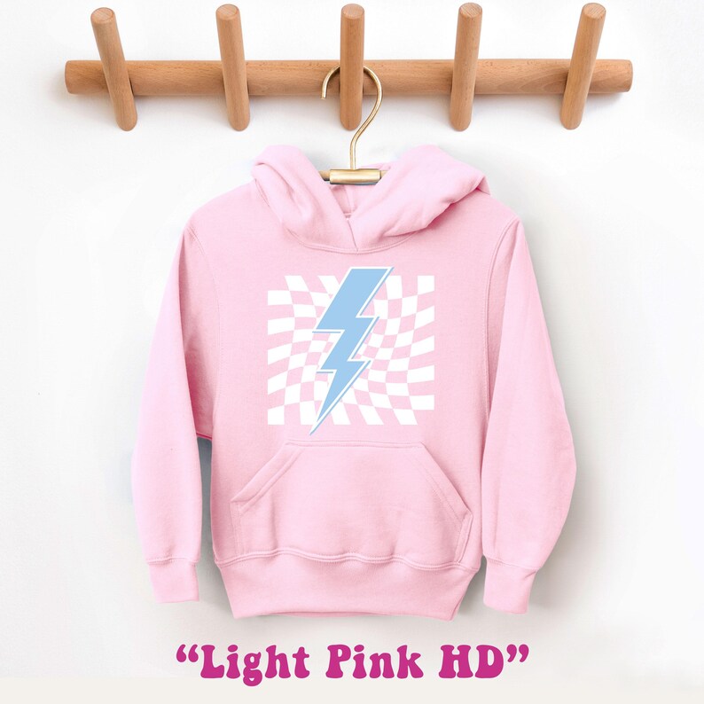 Puede incluir: Una sudadera con capucha rosa claro con un gr&aacute;fico de rayo azul sobre un fondo a cuadros blancos. El texto "Light Pink HD" est&aacute; impreso debajo de la imagen.