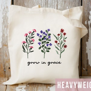 May include: A white tote bag with a floral design and the text "grow in grace". The flowers are pink, purple, and red.