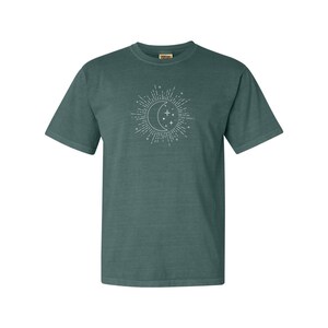 Puede incluir: Una camiseta de manga corta azul turquesa con un gr&aacute;fico blanco de una luna creciente y estrellas.