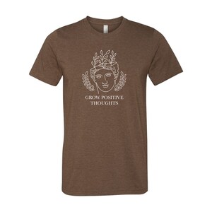 May include: Brown t-shirt with a white outline of a person's head with leaves around it. The text "GROW POSITIVE THOUGHTS" is below the image.