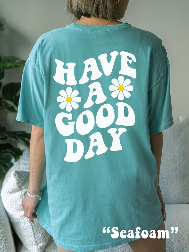 May include: A turquoise blue t-shirt with a white graphic that says "Have a Good Day" with two white daisies on either side of the "a".