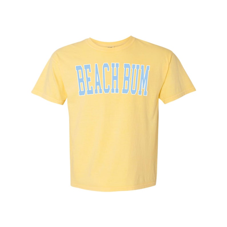 Pu&ograve; includere: Una maglietta gialla a maniche corte con il testo "BEACH BUM" in blu.