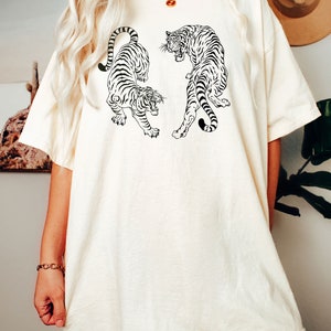May include: A white oversized t-shirt with a black and white graphic of two tigers facing each other. The text "Ivory" is written below the image.