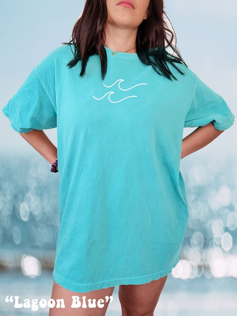 May include: A turquoise blue t-shirt with a white wave graphic. The t-shirt is oversized and has a relaxed fit. The colour of the shirt is described as "Lagoon Blue".