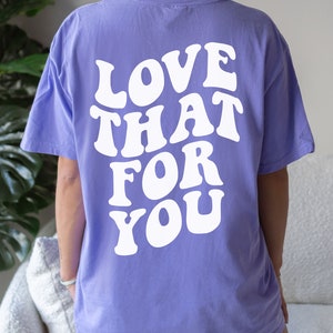 K&ouml;nnte beinhalten: Ein lila T-Shirt mit dem Text "LOVE THAT FOR YOU" in wei&szlig;er, retro-artiger Schrift auf der R&uuml;ckseite. Das Shirt ist mit "Violet" gekennzeichnet.