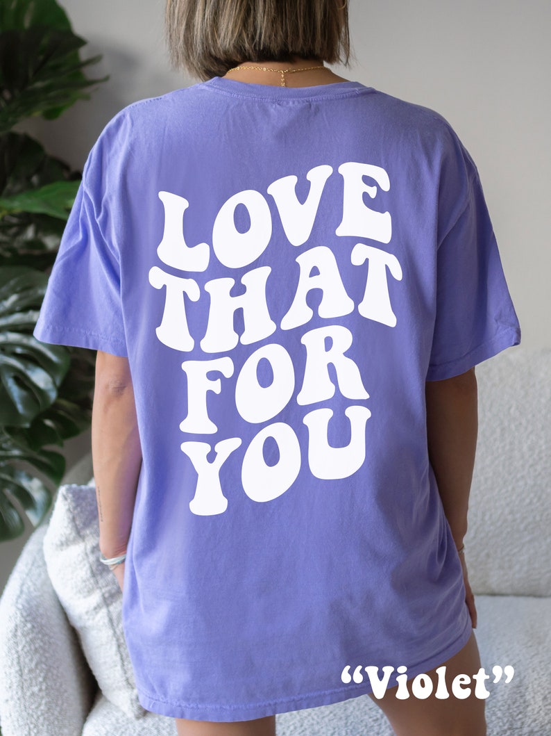 K&ouml;nnte beinhalten: Ein lila T-Shirt mit dem Text "LOVE THAT FOR YOU" in wei&szlig;er, retro-artiger Schrift auf der R&uuml;ckseite. Das Shirt ist mit "Violet" gekennzeichnet.