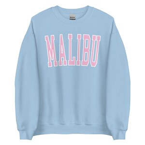 K&ouml;nnte beinhalten: Ein hellblauer Pullover mit dem Wort "MALIBU" in rosa Buchstaben.