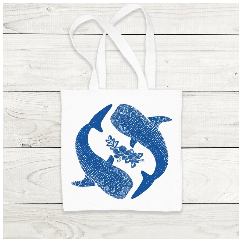 May include: White tote bag with blue whale shark silhouettes and a floral design. The whales are facing each other and have a dotted pattern.