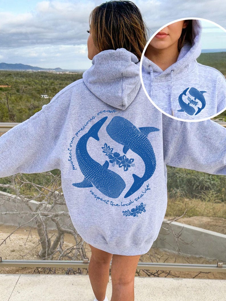 K&ouml;nnte beinhalten: Ein graumelierter Kapuzenpullover mit einer gro&szlig;en blauen Grafik auf der R&uuml;ckseite, die zwei Walhaie in einem Kreis mit Hibiskusbl&uuml;ten und dem Text "protect our precious oceans respect the local sea life" zeigt. Eine kleinere passende Grafik befindet sich auf der Vorderseite.