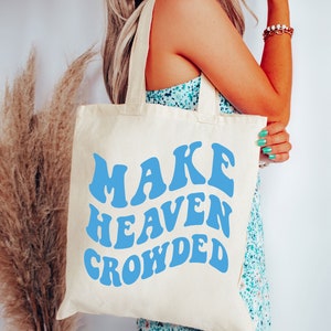 May include: A white canvas tote bag with blue text that reads "MAKE HEAVEN CROWDED".