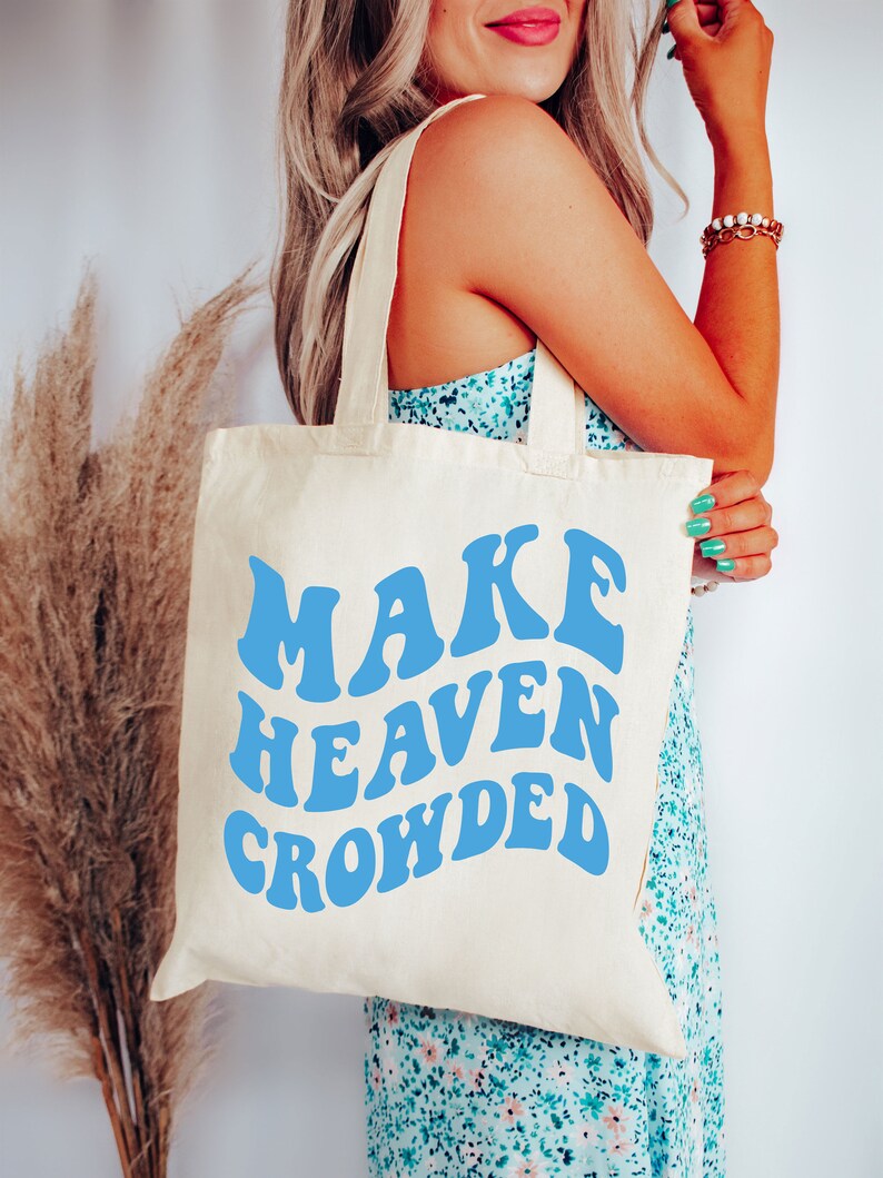 May include: A white canvas tote bag with blue text that reads "MAKE HEAVEN CROWDED".