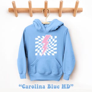 Puede incluir: Una sudadera azul claro con un gr&aacute;fico de rayo rosa sobre un fondo a cuadros blancos. La sudadera tiene capucha y bolsillo canguro. "Carolina Blue HD" est&aacute; escrito debajo de la imagen.