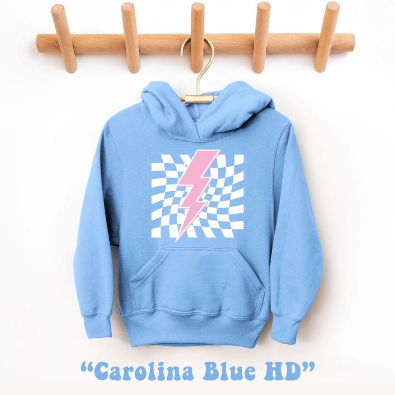Puede incluir: Una sudadera azul claro con un gr&aacute;fico de rayo rosa sobre un fondo a cuadros blancos. La sudadera tiene capucha y bolsillo canguro. "Carolina Blue HD" est&aacute; escrito debajo de la imagen.