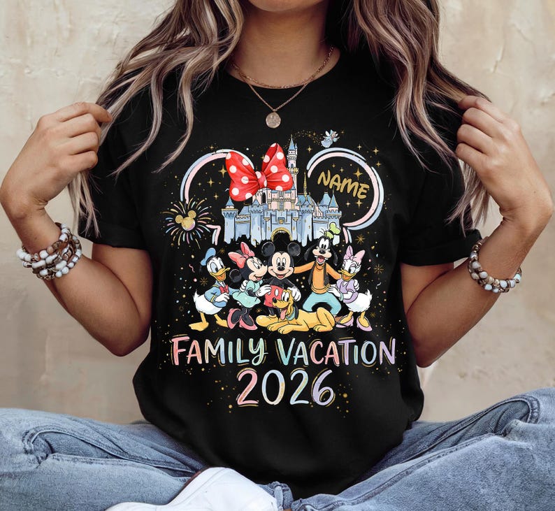 May include: A black short-sleeved t-shirt featuring a colorful graphic of Disney characters including Mickey Mouse, Minnie Mouse, Donald Duck, Daisy Duck, Goofy, and Pluto in front of a castle. The text reads NAME, FAMILY VACATION, and 2026.