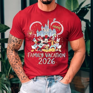 May include: A red short-sleeved t-shirt featuring a graphic of a castle, fireworks, and Disney characters including Mickey, Minnie, Donald, Daisy, Goofy, and Pluto. The text reads "NAME", "FAMILY VACATION", and "2026" in a colorful, stylized font.