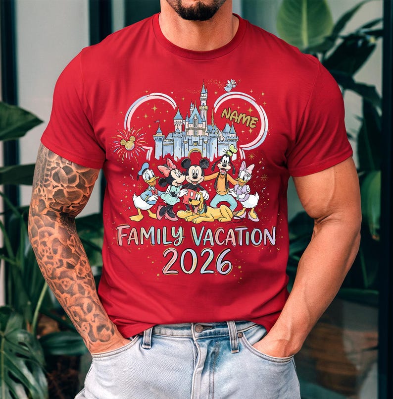 May include: A red short-sleeved t-shirt featuring a graphic of a castle, fireworks, and Disney characters including Mickey, Minnie, Donald, Daisy, Goofy, and Pluto. The text reads "NAME", "FAMILY VACATION", and "2026" in a colorful, stylized font.