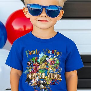 Op de afbeelding: Een kind draagt een blauwe zonnebril en een blauw t-shirt. Het shirt heeft een kleurrijke afbeelding met de tekst "Family Vacation" en "Universal Studios 2026", met stripfiguren.