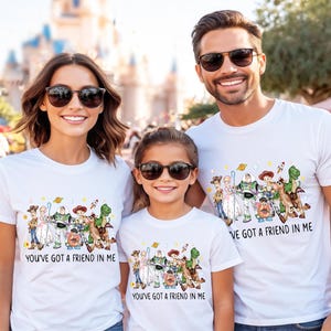 May include: Three people wearing white t-shirts with a colorful graphic of Toy Story characters. The text "YOU'VE GOT A FRIEND IN ME" is printed on the shirts. The people are wearing sunglasses and smiling.