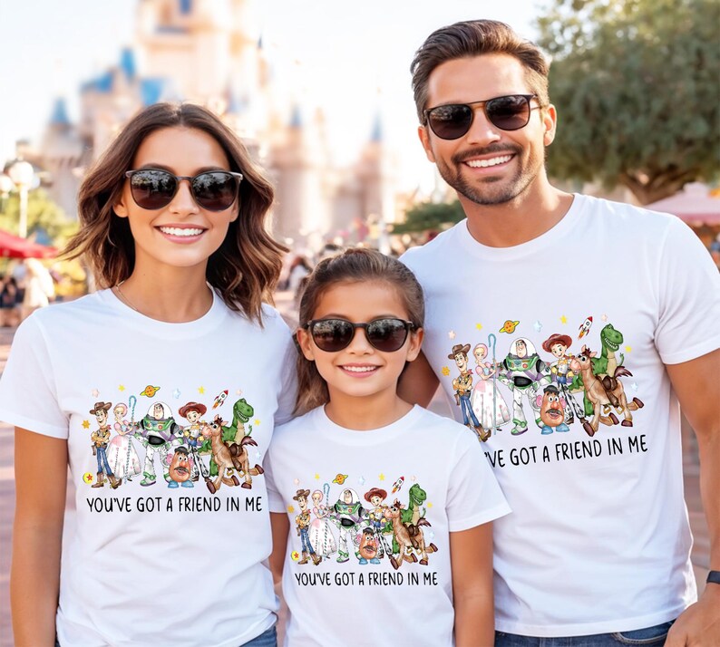 May include: Three people wearing white t-shirts with a colorful graphic of Toy Story characters. The text "YOU'VE GOT A FRIEND IN ME" is printed on the shirts. The people are wearing sunglasses and smiling.