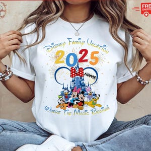 May include: White t-shirt with a colorful graphic of Mickey Mouse and friends in front of Cinderella's Castle. The text "Disney Family Vacation 2025" is above the graphic and "Where the Magic Begins!" is below.