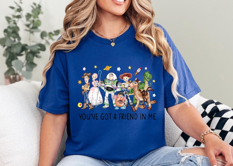 May include: A royal blue t-shirt featuring a colorful graphic of Toy Story characters, including Woody, Buzz Lightyear, and others. The text "YOU'VE GOT A FRIEND IN ME" is printed below the characters. The shirt is a comfortable, casual style.