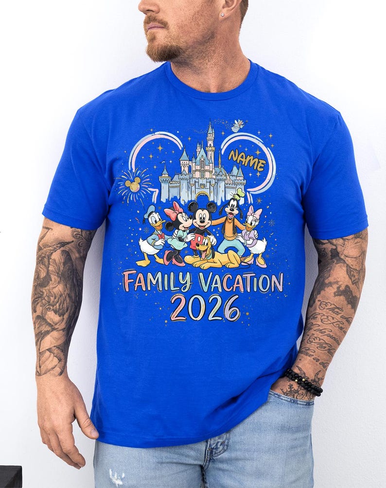 May include: A royal blue short-sleeve t-shirt featuring a colorful graphic of Disney characters including Mickey, Minnie, Donald, Daisy, Goofy, and Pluto in front of a castle. The text reads "NAME", "FAMILY VACATION", and "2026" in a playful font.