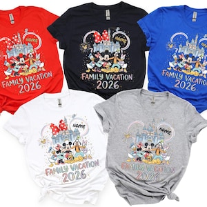 May include: Five short-sleeved t-shirts in red, black, blue, white, and gray. Each features a graphic of cartoon characters in front of a castle with fireworks, the text "NAME", "FAMILY VACATION", and "2026" printed in a colorful, stylized font.