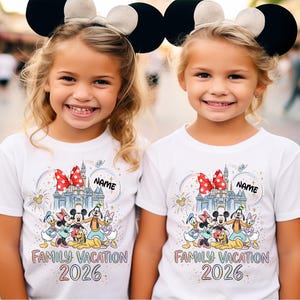 May include: Two white short-sleeved t-shirts featuring a colorful graphic of a castle, a red polka-dot bow, and cartoon characters including Mickey, Minnie, Donald, Daisy, Goofy, and Pluto. The text reads "NAME", "FAMILY VACATION", and "2026".