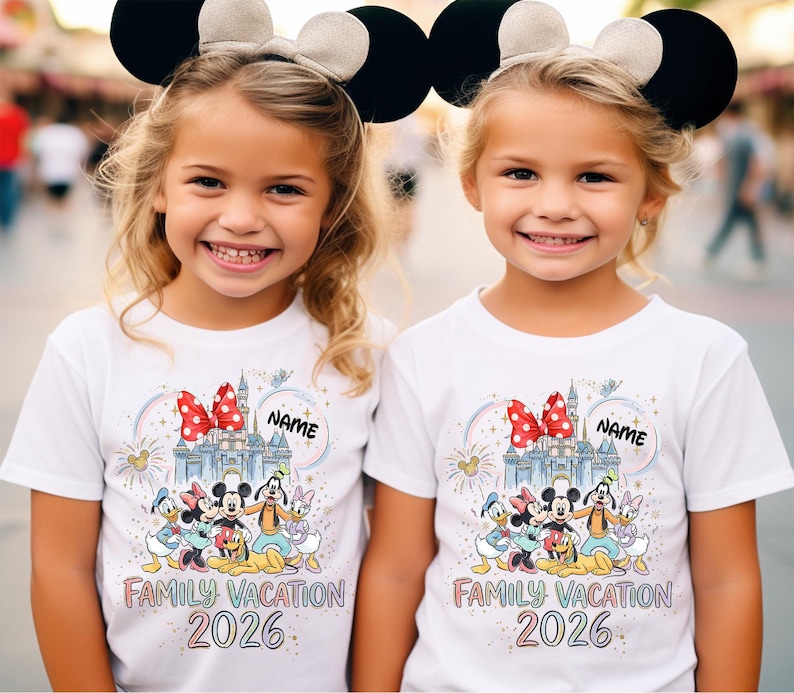 May include: Two white short-sleeved t-shirts featuring a colorful graphic of a castle, a red polka-dot bow, and cartoon characters including Mickey, Minnie, Donald, Daisy, Goofy, and Pluto. The text reads "NAME", "FAMILY VACATION", and "2026".
